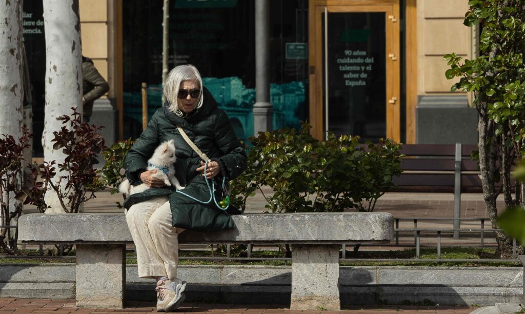 Mujer mayor sentada en un banco con su perro en una mañana soleada en Logroño, captada en una escena cotidiana por RSBlogging.
