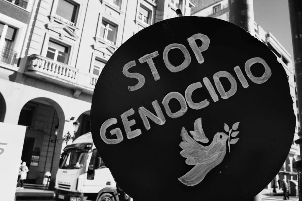 Pancarta circular negra con el mensaje “Stop Genocidio” y una paloma blanca con una rama de olivo, durante una manifestación en la ciudad. Fotografía en blanco y negro por RSBlogging.