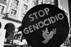 Pancarta circular negra con el mensaje “Stop Genocidio” y una paloma blanca con una rama de olivo, durante una manifestación en la ciudad. Fotografía en blanco y negro por RSBlogging.